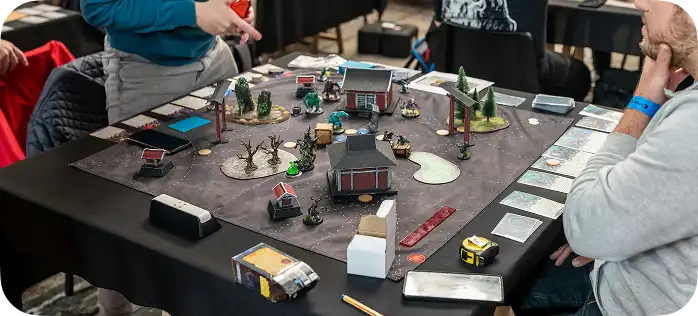 Spelers aan de tafel tijdens een tactisch spel met miniatuurgebouwen, bomen en figuurtjes van personages.